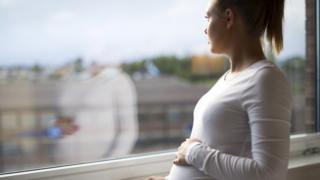 Беременная женщина смотрит в окно