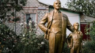 Una estatua de Lenin y de un niño frente a una casa