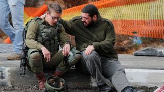 An Isreali soldier is consoled as Israeli forces and forensic experts inspect the site of a Palestinian drive-by shooting attack outside the West Bank settlement of Givat Asaf, northeast of Ramallah, on December 13, 2018
