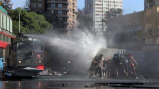 A riot police water cannon sprays water towards demonstrators during a protest in Santiago.