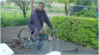 Bernard Kiwia outside on a bicycle which runs a water-pump