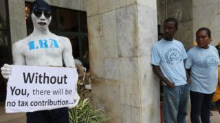 A comedian holds a tax information poster during Taxpayers Appreciation Day at the Monrovia City Hall in Monrovia, Liberia, 01 July 2017.