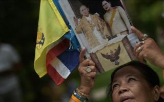 Тайский доброжелатель держит фотографию тайского короля Пумипона Адульядета и королевы Сирикит, когда она возносит молитвы за его выздоровление в больнице Сирирадж в Бангкоке 6 октября 2014 года.