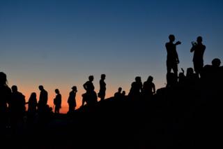 Silhouettes of people watching a sunset atop the Aeropagus hill in Athens