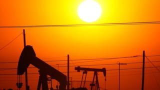 Imagem alaranjada de um pôr-do-Sol por trás de uma instalação petrolífera