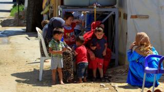 Сирийские беженцы сидят со своими детьми возле палаток в лагере в восточном ливанском городе Сааднаэль (19 июля 2016 года)