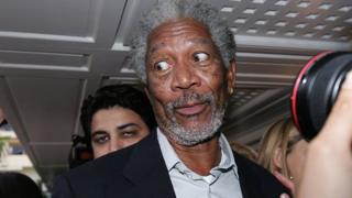 Morgan Freeman mira hacia un lado, como con sorpresa mientras los periodistas lo abordan.