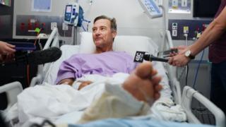 Neil Parker habla con reporteros desde cama del hospital
