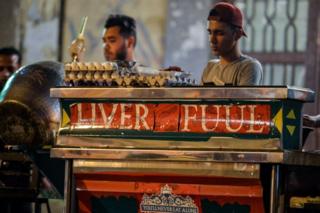 Egyptians cook food during the pre-dawn "suhur" meal before a new day of fasting begins, early on 31 May, near a food cart labelled "Liver Fuul", a play on Arabic name for fava beans and English football club Liverpool FC, in the Ain Shams suburb of Cairo. Egyptian football fans readied to cheer on national hero Mohamed Salah in Sunday's Champions League clash and tuck into food from a cart whose owner vows they'll "never eat alone". A tribute to the Reds, the "Liverfuul" cart serves up hot dishes of "fuul" (fava beans) in Ain Shams, a working-class suburb of Cairo.