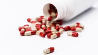 Many red and transparent medical capsules, filled with yellow medicine, pouring out of a white container