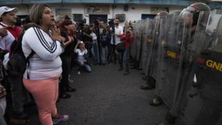 Эта женщина и группа людей пытаются убедить Национальную гвардию Венесуэлы пропустить их на территорию Колумбии