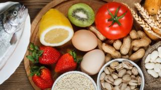 Food allergy concept. Almonds, milk, pistachios, tomato, lemon, kiwi, trout, strawberry, bread, sesame seeds, eggs, peanuts and bean on wooden table