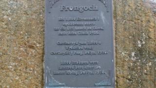 Cofeb yn y pentre', mewn Gaeleg, Cymraeg a Saesneg, sy'n nodi hanes y gwesyll