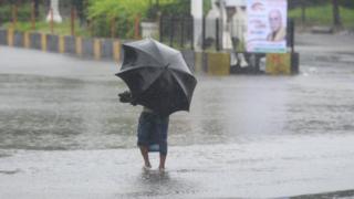 A man with an umbrella wades through floodwater in Khulna, Bangladesh