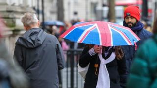 Женщина укрывается от дождя под зонтиком Union Jack во время дождя в центре Лондона.