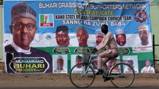 A cyclist drives pasts a campaign poster for President Muhammadu Buhari