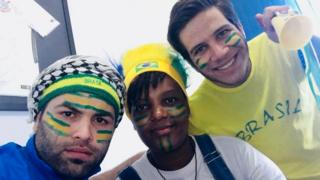 A moçambicana Lara Lopes vendo o jogo Brasil x México com dois amigos sírios