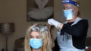 A hairdresser wearing a face visor treats a woman's hair