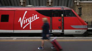 A passenger walking with a suitcase alongside a Virgin train