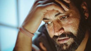 Bearded man holding his head in his hand and tearing up