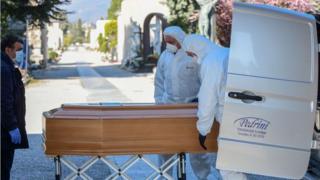 Undertakers wearing protective clothing carry a coffin in a cemetery in Bergamo