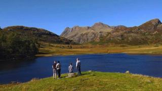 Four tourists admire the view (hills and lake) in the Lake District