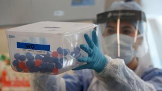 A laboratory technician holds a container of test tubes containing coronavirus test samples