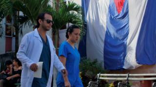 Dos profesionales de la salud pasan por delante de una bandera cubana en el hospital Calixto Garcia de La Habana