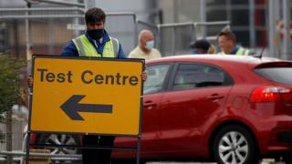 A man putting out a sign to direct people to a mobile testing center in Bolton, England.