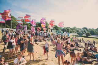 Crowd of people at Glastonbury Festival 2017, with flags and trees in the distance