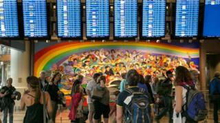 Pessoas olham para telas de chegadas e partidas em aeroporto