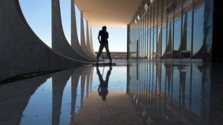 Sombra de pessoa limpando chão da varanda do prédio do STF durante o dia