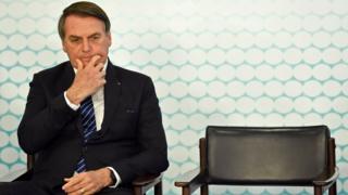 Bolsonaro sentado em cadeira durante evento olhando para baixo