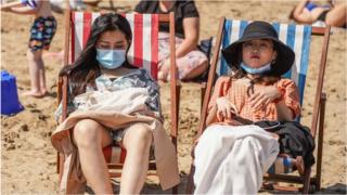 Gente en la playa con mascarillas.