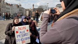 Женщина фотографирует демонстрантов, держащих плакат с надписью «Нет запретным мерам» во время акции протеста 27 марта 2010 года в Брюсселе против запрета мусульманских платков в школах