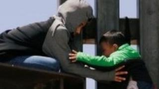 A small boy is passed over a border wall in the US.