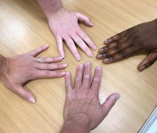 Four people lay their hands on a table