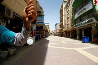 A man holds a pocket watch at noon, in front of an almost empty market near the Imam Ali shrine in Najaf, Iraq