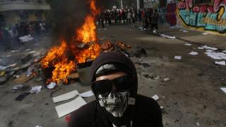 A demonstrator wears a mask and stands in front of a fire