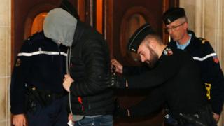 An unnamed defendant arrives hiding his face at Paris courthouse