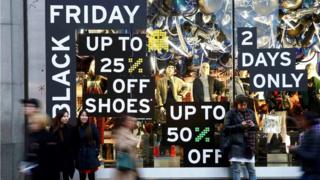 Shoppers walk past a store promoting "Black Friday" in London