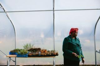 A participant stands in a polytunnel next to a table of plants