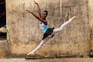 A teenage girl performs a ballet jump outside the classroom.