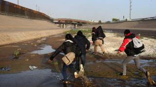 A group of people run at the Rio Bravo, at the Paso del Norte checkpoint, in Ciudad Juarez