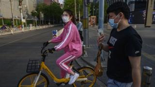 Chineses andando de bicicleta e a pé em rua quase deserta