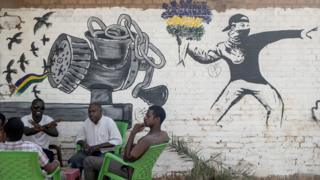 People drinking tea or coffee in front of a mural drawn in the style of Banksy - Khartoum, Sudan