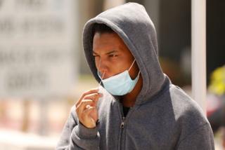 A young man in a hoodie adminsters a swab test on himself