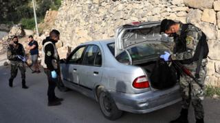 Three armed security officers go through a vehicle on the side of the road