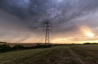 Dark clouds over a pylon in a field