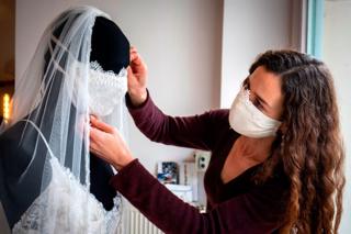 A woman adjusts the face mask on a mannequin that is wearing a wedding dress